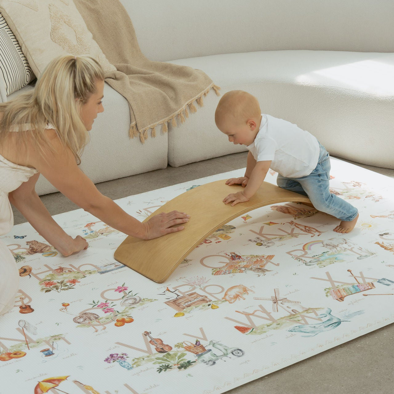 Woman and baby playing on a colorful play mat in a living room.