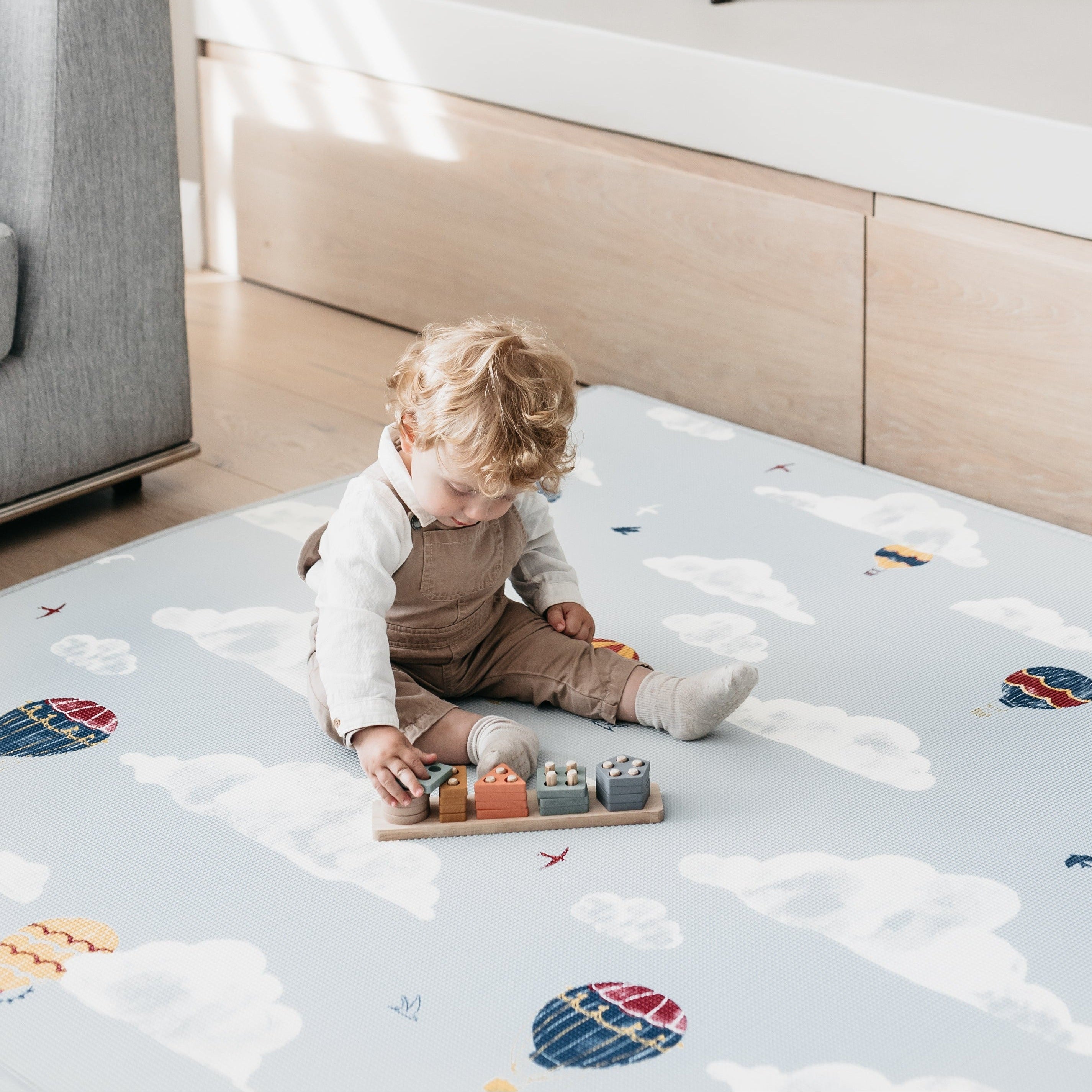 Child playing on a colorful play mat with toys in a room.
