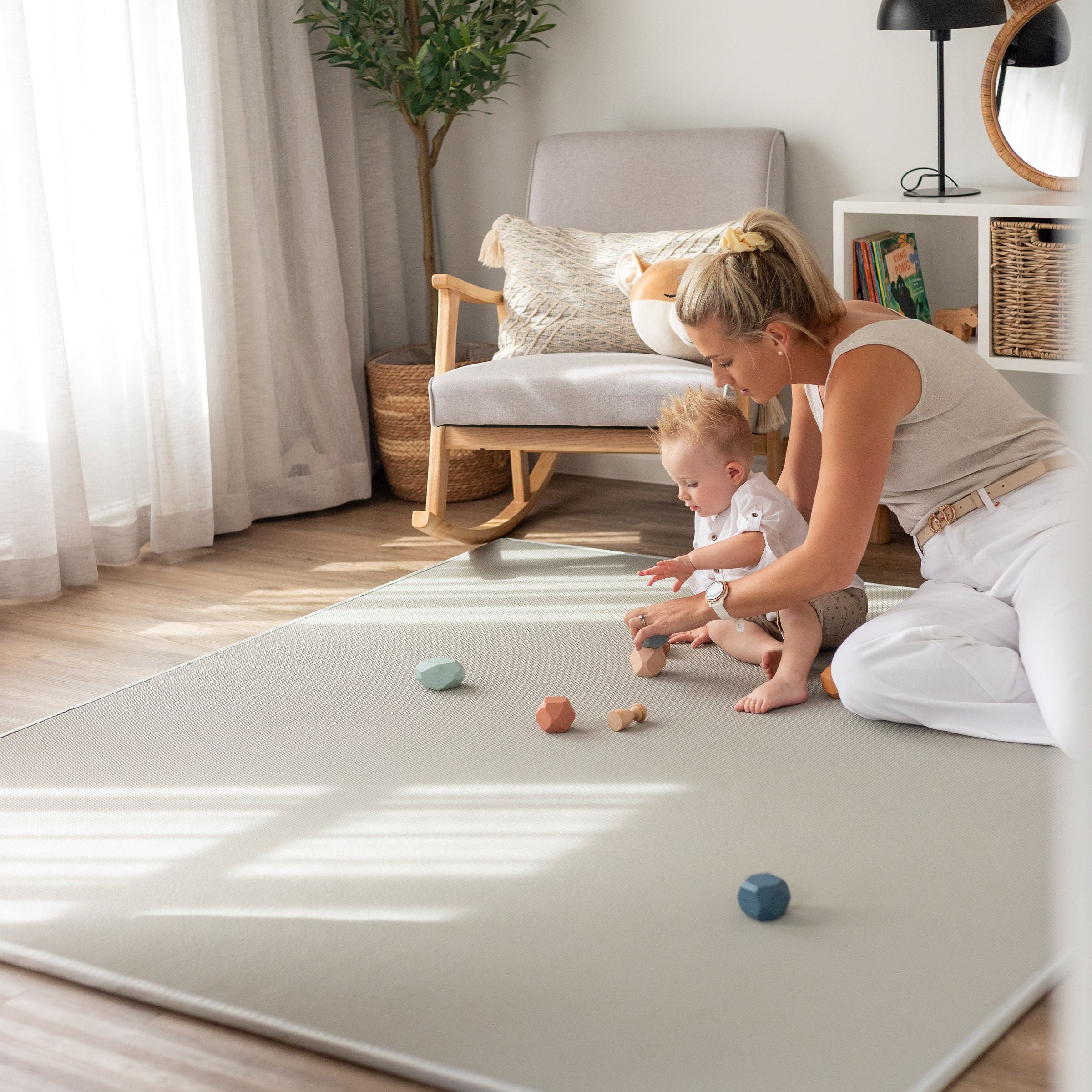 Woman and child playing on a large white mat in a bright living room.